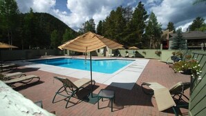 A swimming pool with lounge chairs and a covered area, surrounded by trees and a mountain backdrop. - Flying Dutchman 1 Bedroom Apartment by Key to the Rockies (Keystone)