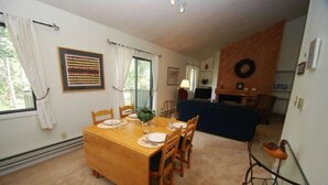A dining area with a wooden table set for four, a blue sofa, and a kitchen area with a wooden wall and a wreath. - Flying Dutchman 1 Bedroom Apartment by Key to the Rockies (Keystone)
