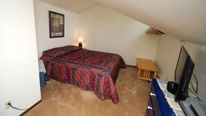 A small, single-bed room with a patterned bedspread, a bedside table, a lamp, a desk with a computer, and a television. - Flying Dutchman 1 Bedroom Apartment by Key to the Rockies (Keystone)