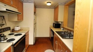 A compact kitchen with wooden cabinets, a stove, a microwave, and a sink.
