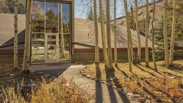 A modern building with a large glass door, surrounded by trees and a sloped landscape.