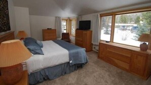 A bedroom with a bed, dresser, TV, and large windows. - Pines Condominiums 3 Bedroom Apartment by Key to the Rockies (Keystone)