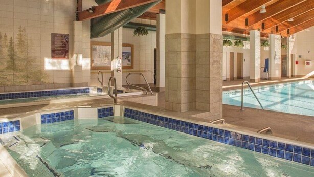 An indoor swimming pool with clear water, wooden beams, and tiled walls. - Pines Condominiums 3 Bedroom Apartment by Key to the Rockies (Keystone)