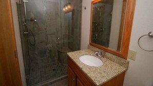 A bathroom with a glass-enclosed shower, a granite countertop sink, and a wooden vanity. - Pines Condominiums 3 Bedroom Apartment by Key to the Rockies (Keystone)