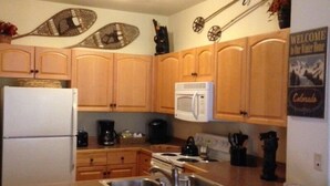 Une cuisine avec des meubles de rangement en bois, un réfrigérateur blanc, un four à micro-ondes et une machine à café.
