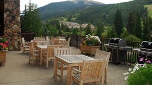 Une terrasse extérieure avec des tables et des chaises en bois, un pilier en pierre et une vue sur une montagne et un chalet.
