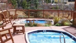 A pool area with wooden chairs and a view of a forested hillside.