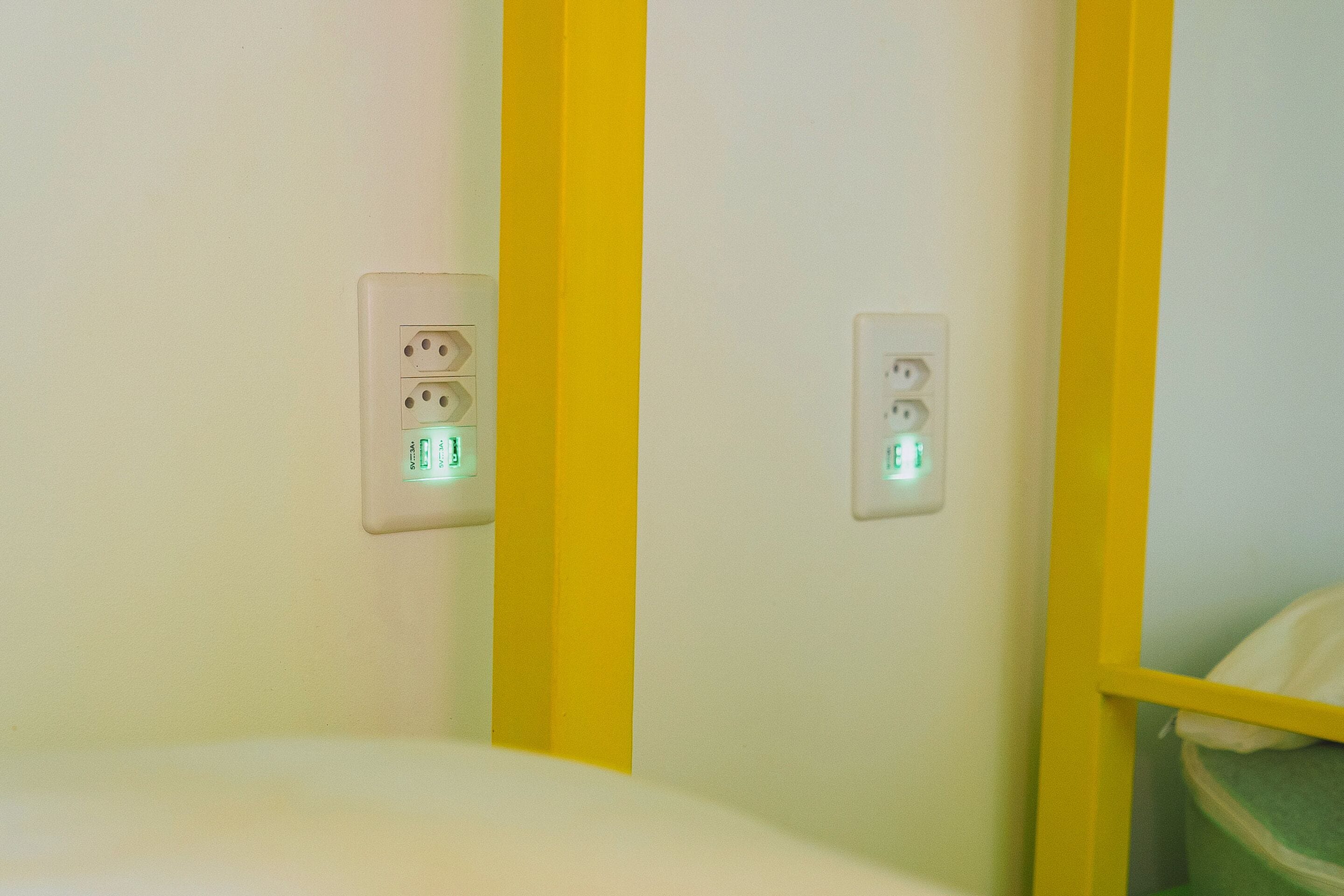 Una habitación con una cama, una pared amarilla y dos enchufes con luces verdes.