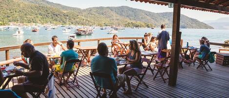A wooden deck with tables and chairs overlooking a marina with boats and hills in the background.