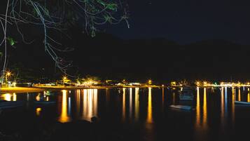 Vista nocturna de un lago tranquilo con barcos y luces distantes reflejándose en el agua.