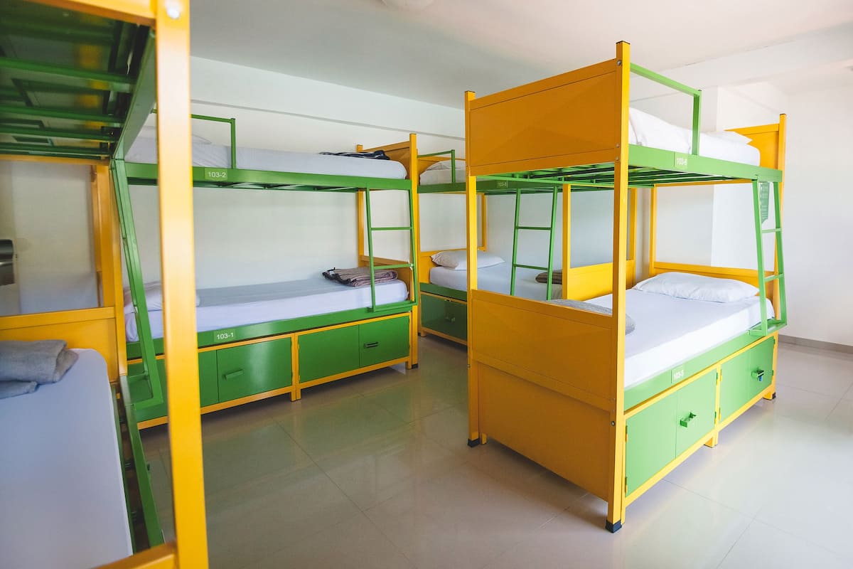 A dormitory room with bunk beds, green and yellow color scheme, and a clean, tiled floor.