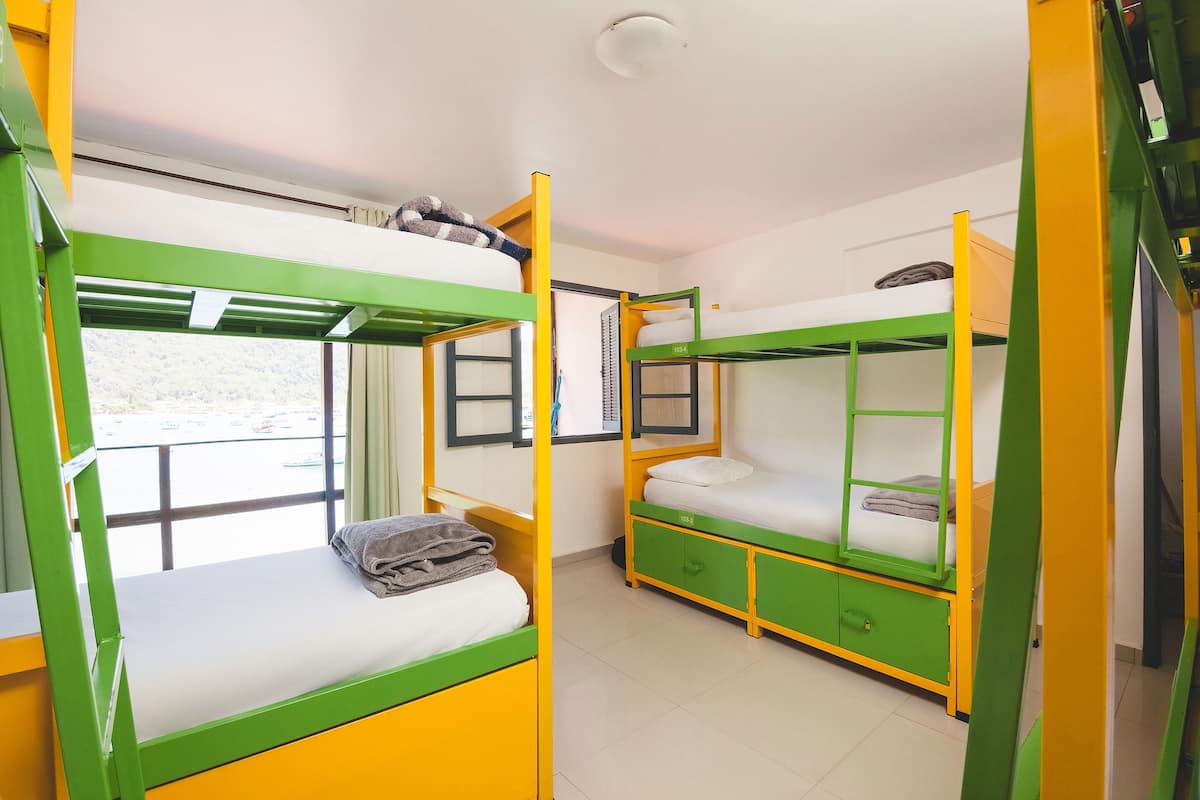 A dormitory room with bunk beds, a window, and a door.