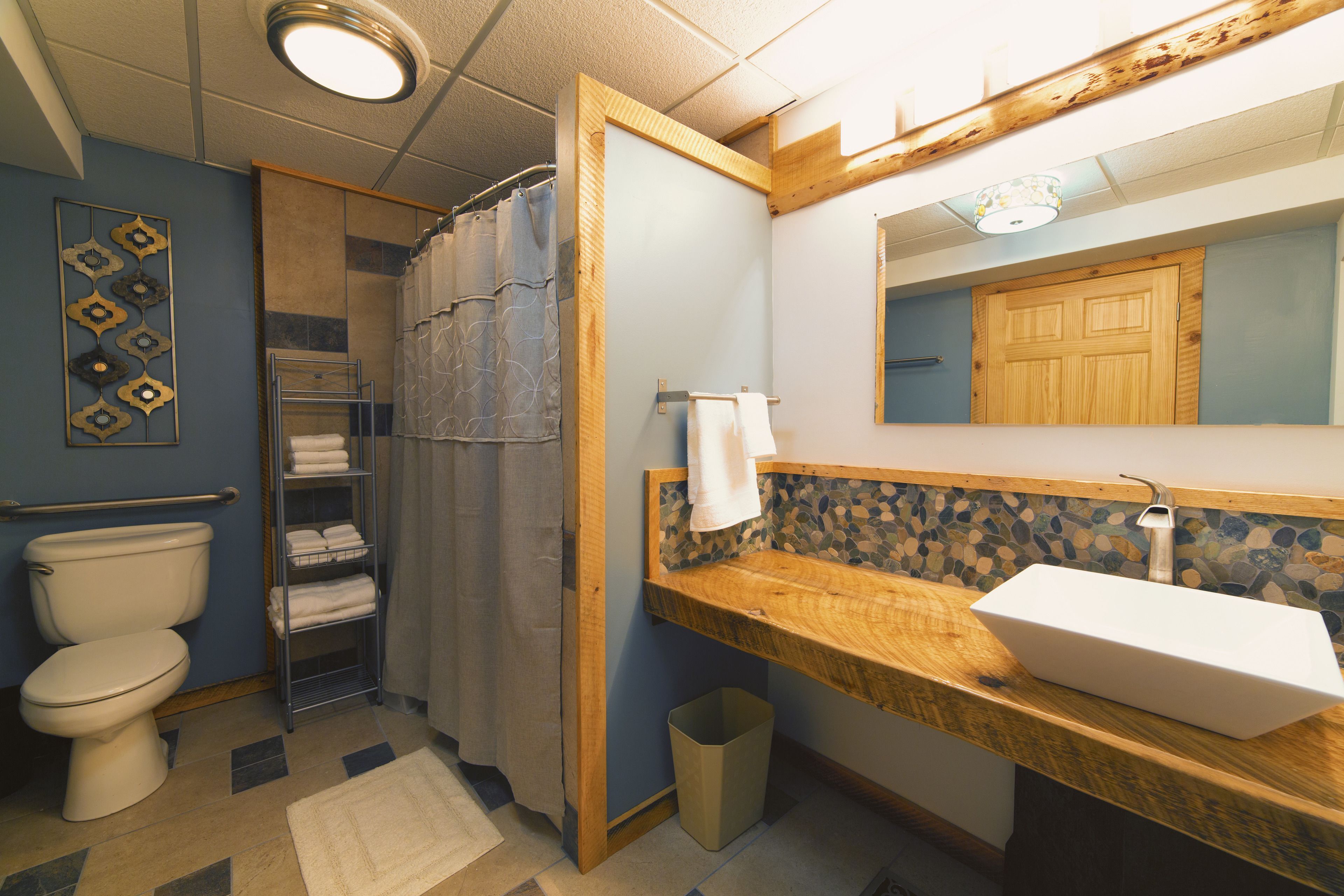 A bathroom with a wooden vanity, a white sink, a shower curtain, a towel rack, and a toilet.