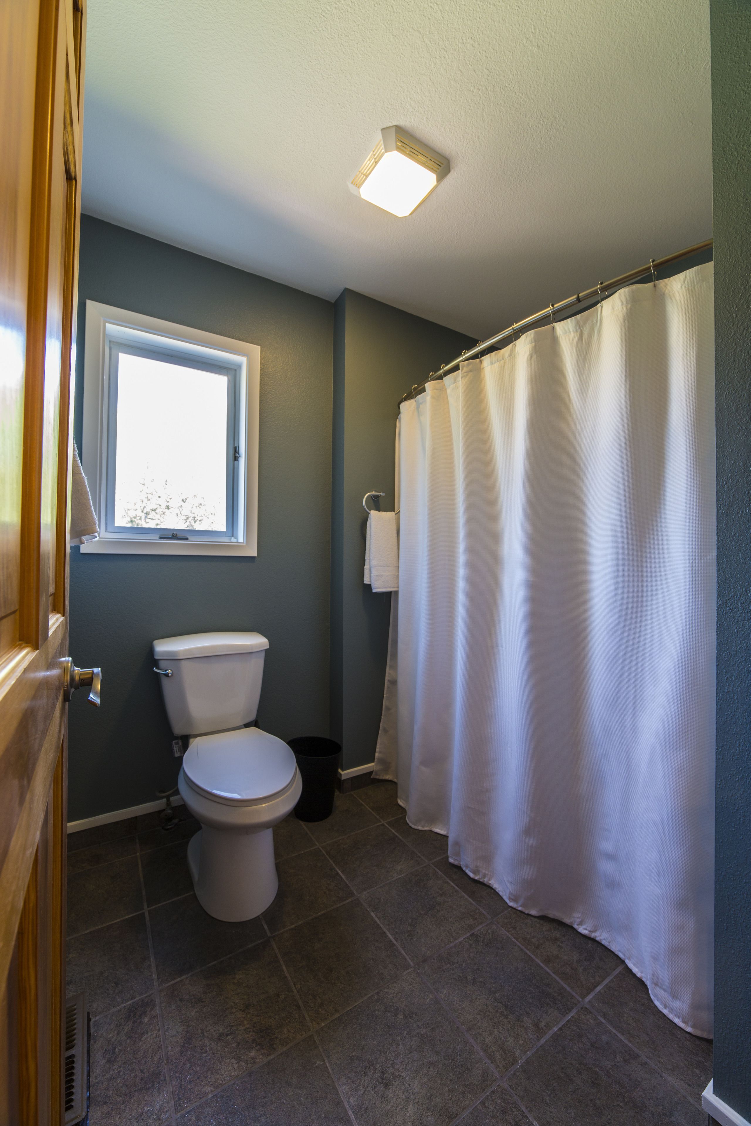 A bathroom with a toilet, a window, a shower curtain, and a towel rack.