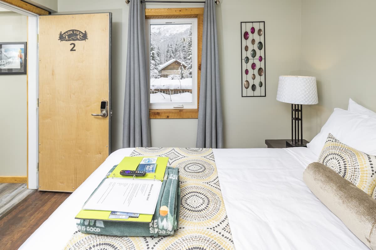 A hotel room with a bed, a window with curtains, a lamp, and a wall decoration.