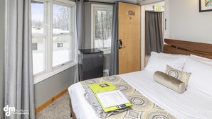 A hotel room with a bed, a desk, and a window with curtains. - Ski Inn (Girdwood)