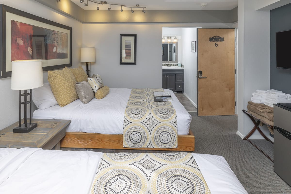 A hotel room with a bed, bedside table, lamp, and a door leading to a bathroom.