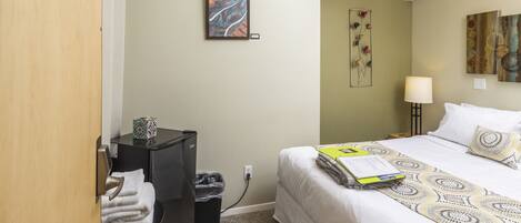 A hotel room with a bed, a desk, a trash bin, and artwork on the walls.