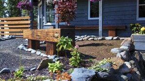 A wooden bench, a flower bed, and a building with a porch. - Ski Inn (Girdwood)