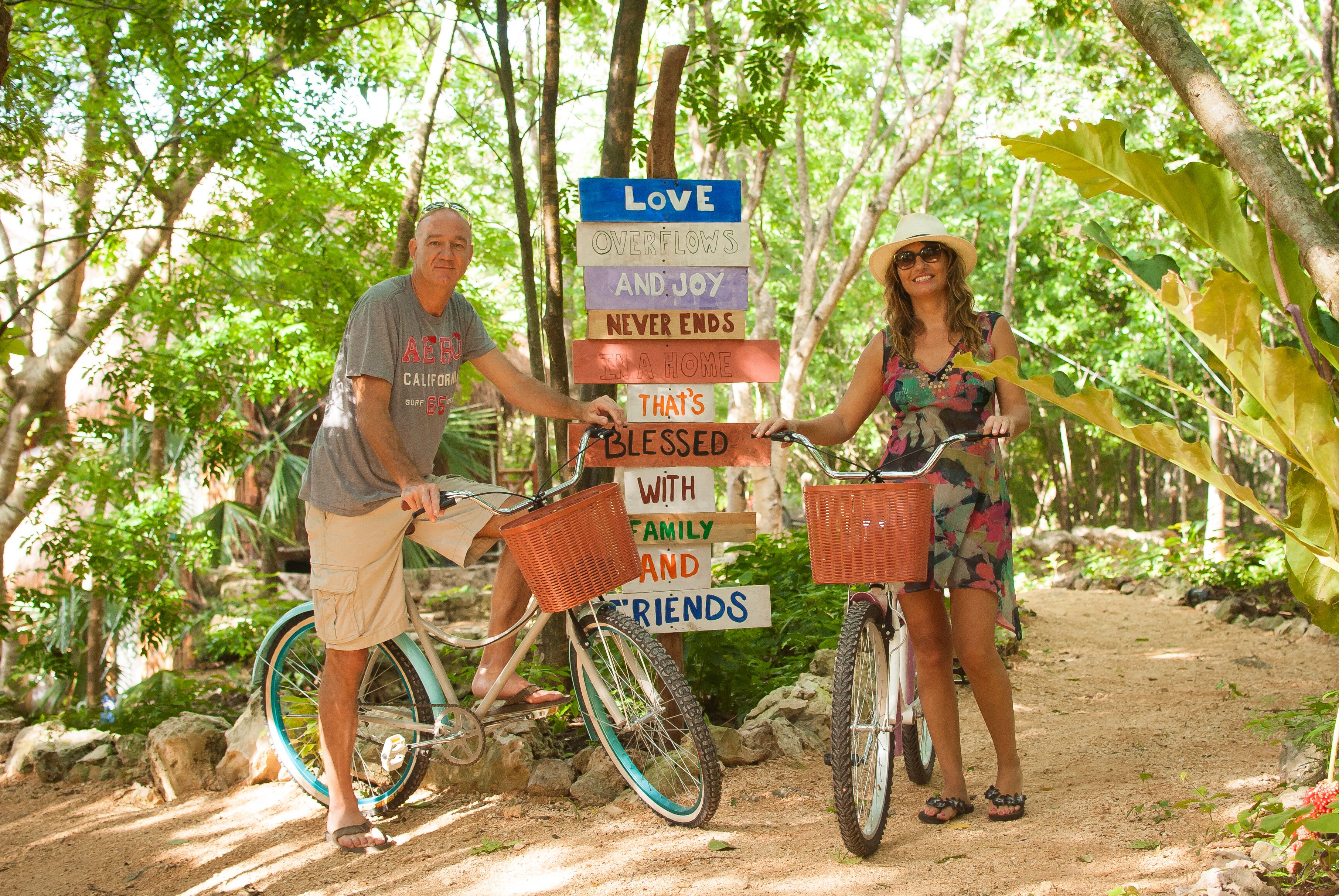 Two people standing next to bicycles with a signpost in a forested area.