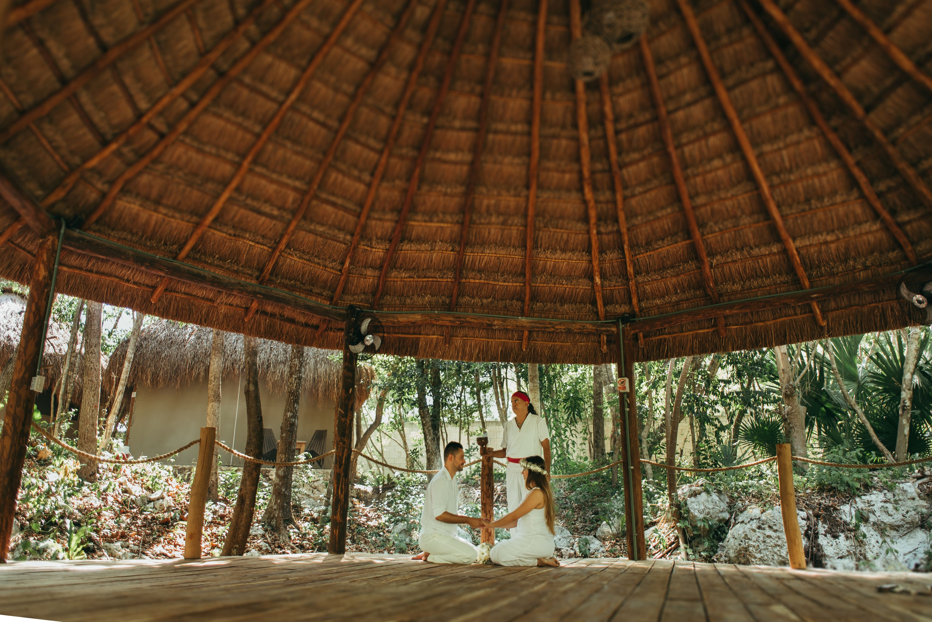 A wooden gazebo with a thatched roof, surrounded by tropical vegetation.