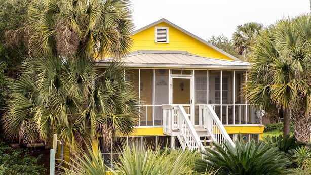 A yellow house with a porch, surrounded by palm trees and other greenery. - E ARCTIC 412 2 Bedroom Holiday Home By My Ocean Rentals (Folly Beach)