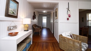 A hallway with a white wall, a wooden floor, a wicker chair, a wicker basket, and a framed picture. - E ARCTIC 412 2 Bedroom Holiday Home By My Ocean Rentals (Folly Beach)