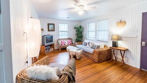A cozy living room with a television, wicker furniture, and a ceiling fan. - E ARCTIC 412 2 Bedroom Holiday Home By My Ocean Rentals (Folly Beach)