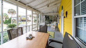 A covered outdoor area with a wooden table and chairs, large windows, and a yellow wall. - E ARCTIC 412 2 Bedroom Holiday Home By My Ocean Rentals (Folly Beach)