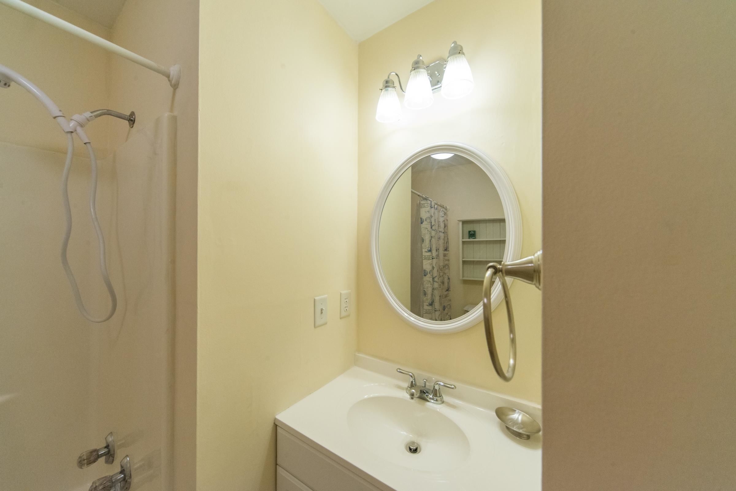 A bathroom with a white sink, a mirror with lights, and a shower area.