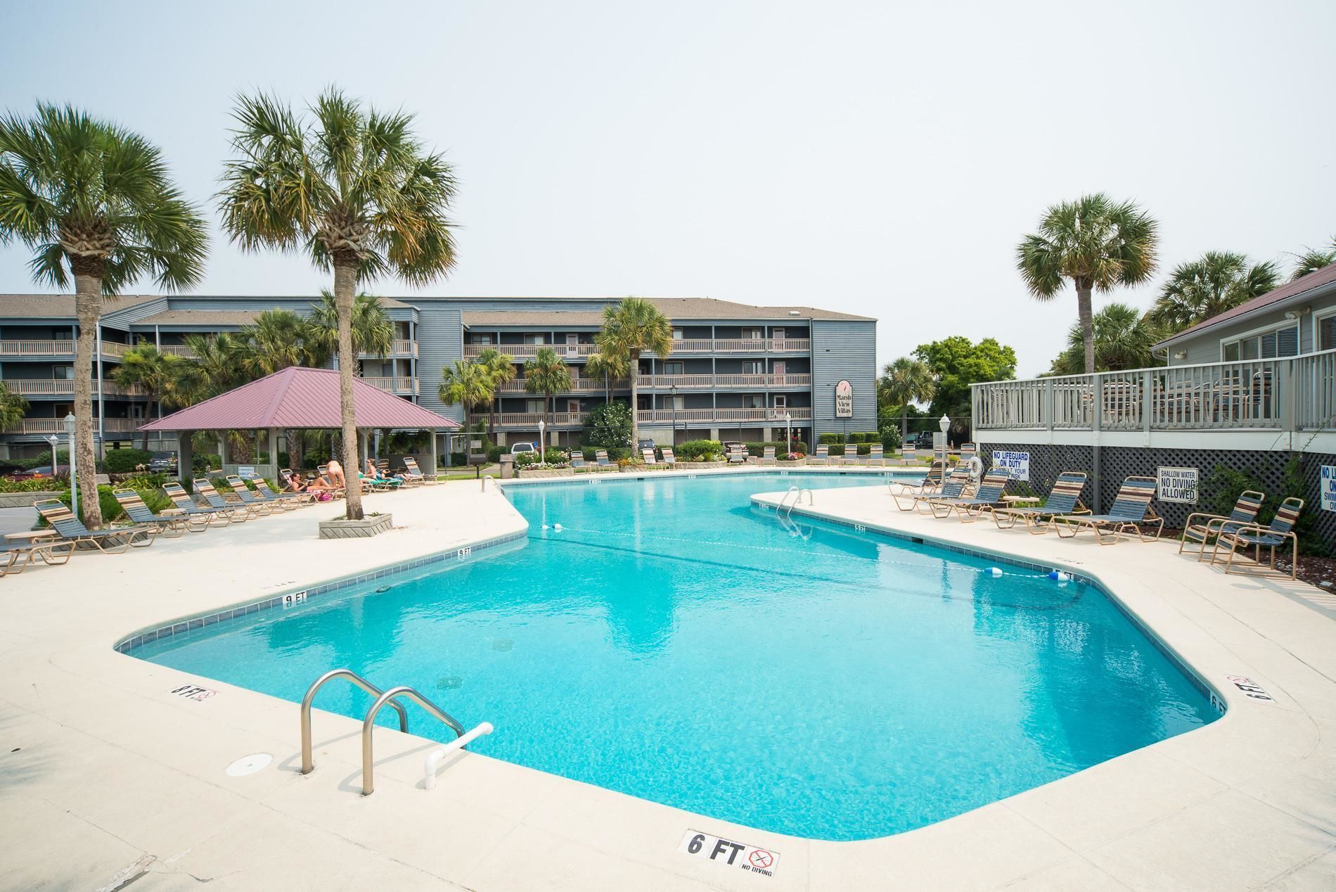 A swimming pool with lounge chairs and palm trees, surrounded by a building with balconies.