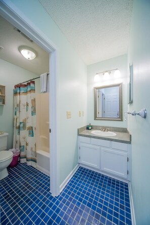 A bathroom with a blue-tiled floor, a white sink, a mirror, and a shower curtain with a palm tree pattern.
