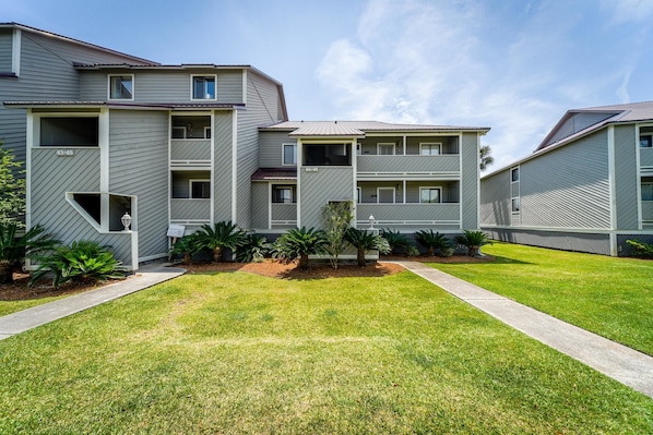 A multi-story residential building with a flat roof, a central courtyard with a small tree, and a well-maintained lawn.