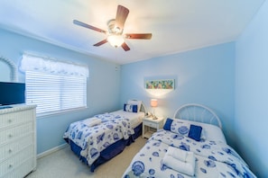 A bedroom with two beds, a ceiling fan, a dresser, a window with blinds, and a painting on the wall.
