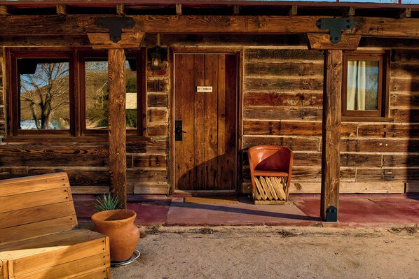 A rustic wooden cabin with a wooden bench, a large planter, and a door with a sign.