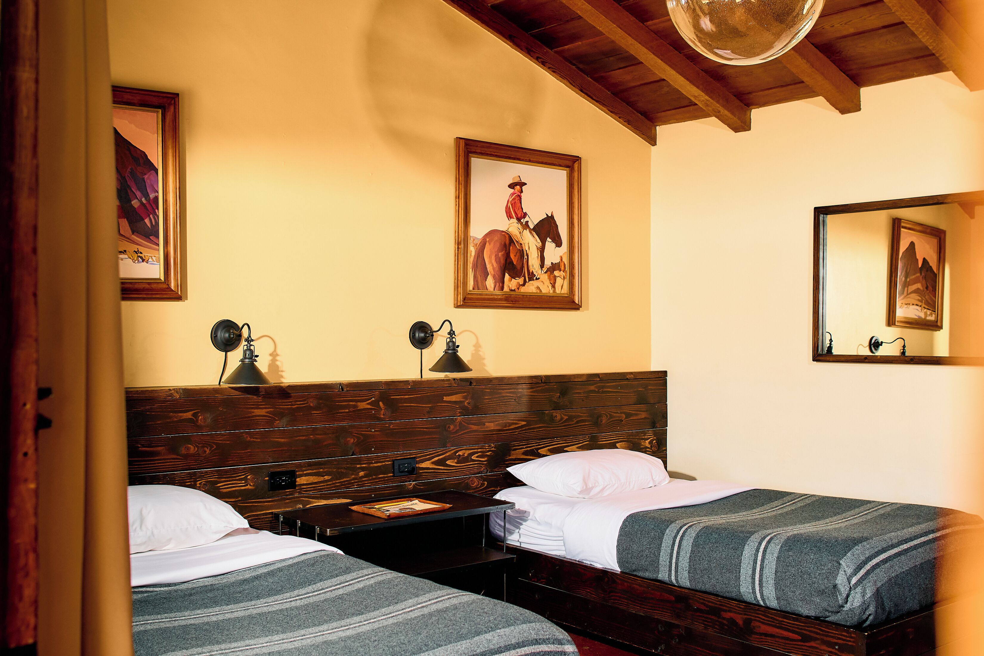 A room with two single beds, wooden headboards, a wooden ceiling, and two wall-mounted lamps.