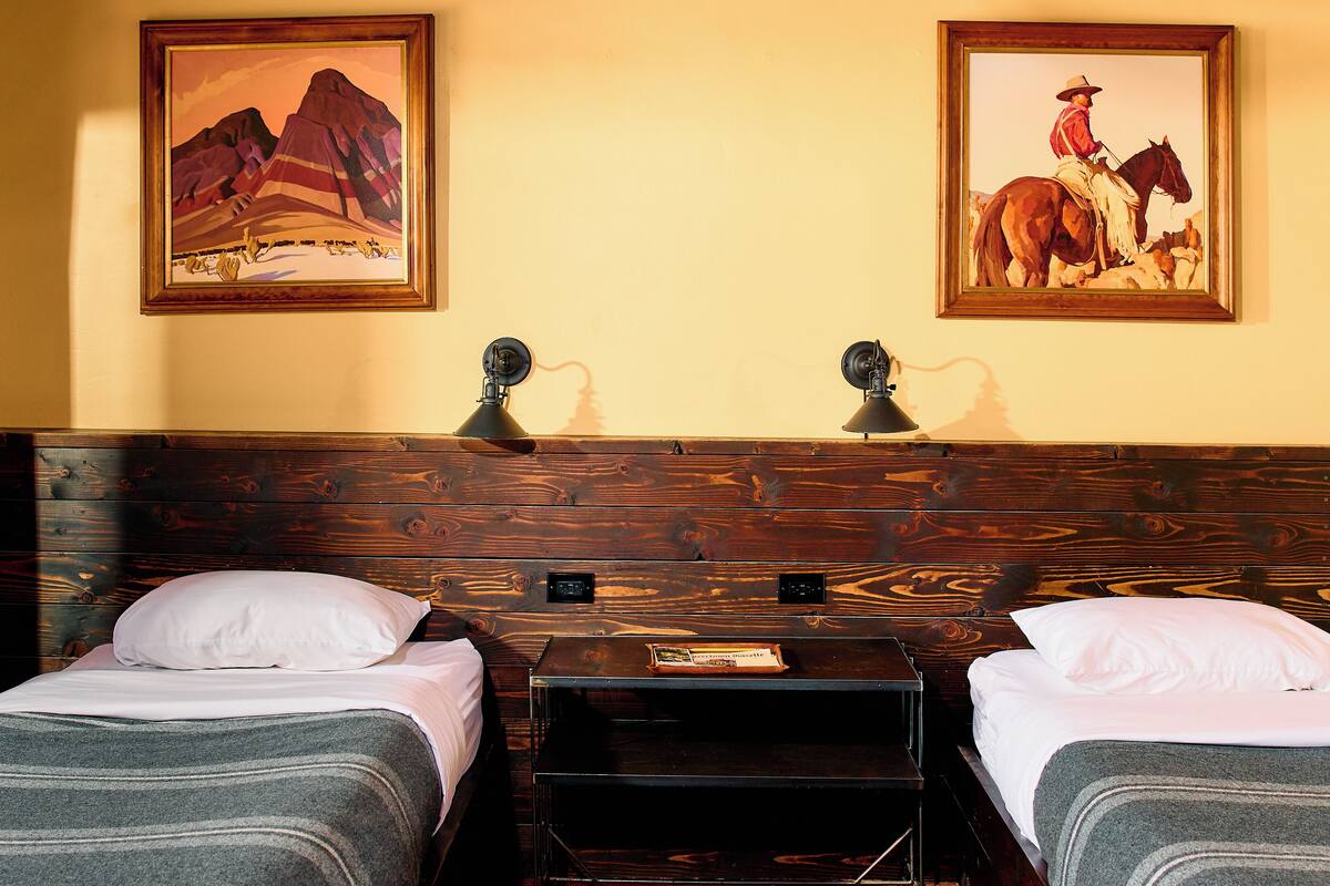 Ein Hotelzimmer mit zwei Betten, einem Holzkopfstück, zwei Wandleuchten und zwei gerahmten Bildern.