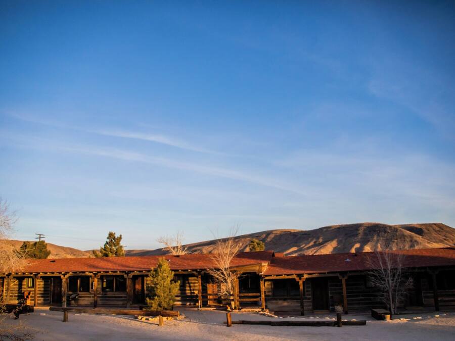A rustic log cabin with a snow-covered ground and a clear blue sky.