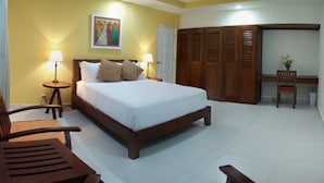 A hotel room with a large bed, two bedside lamps, a wooden wardrobe, a desk with a chair, and a painting on the wall.