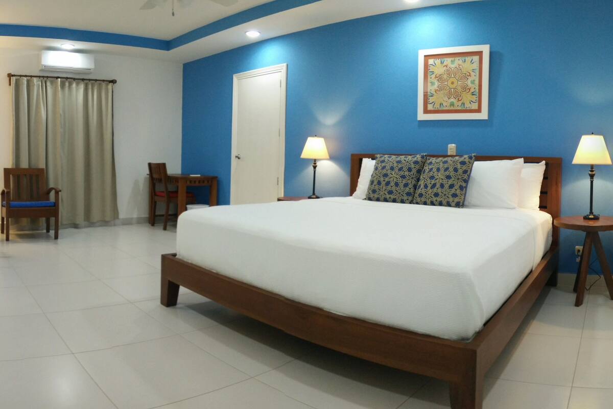 Une chambre d’hôtel avec un grand lit, deux tables de chevet avec des lampes, une chaise, un bureau et une fenêtre avec des rideaux.