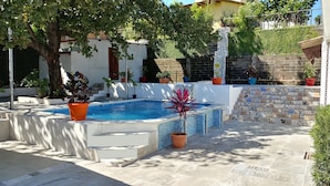 A swimming pool with tiled steps, surrounded by potted plants and a stone wall.