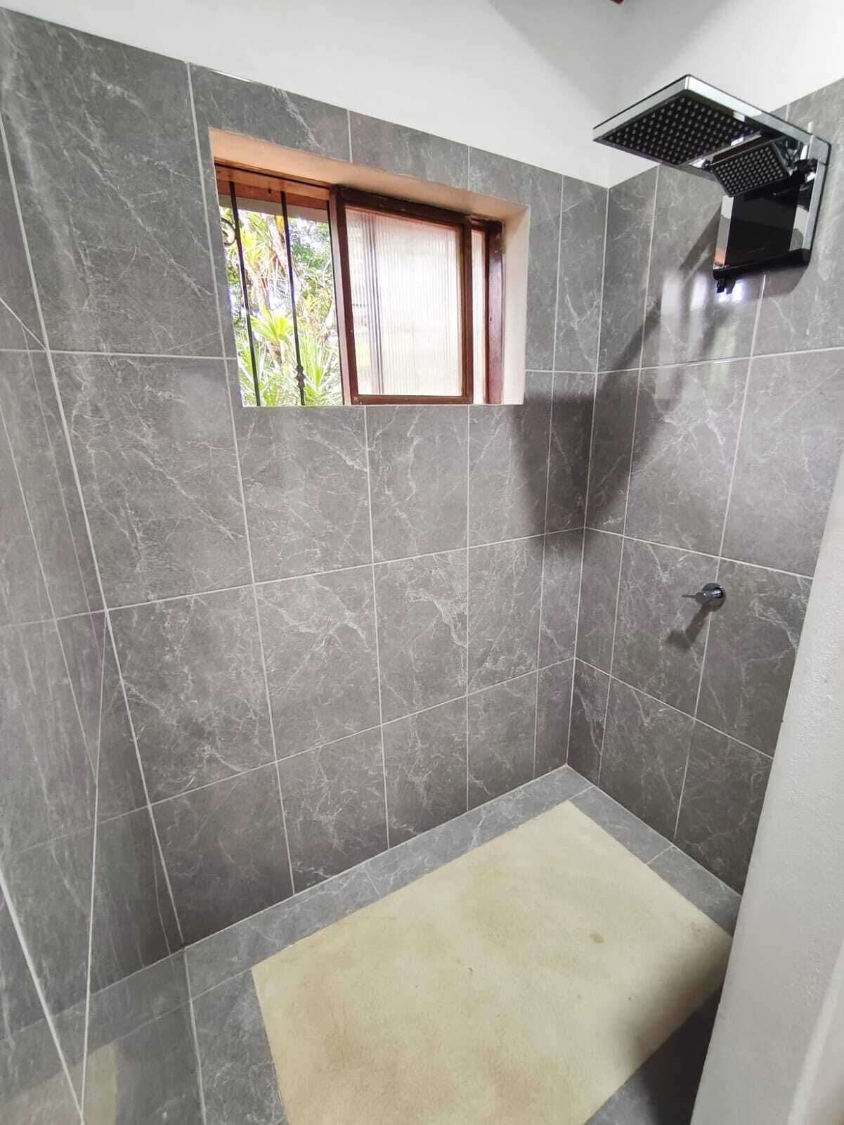 Ein Badezimmer mit grauen Marmorfliesen, einem Fenster mit Holzrahmen und einem Duschbereich.