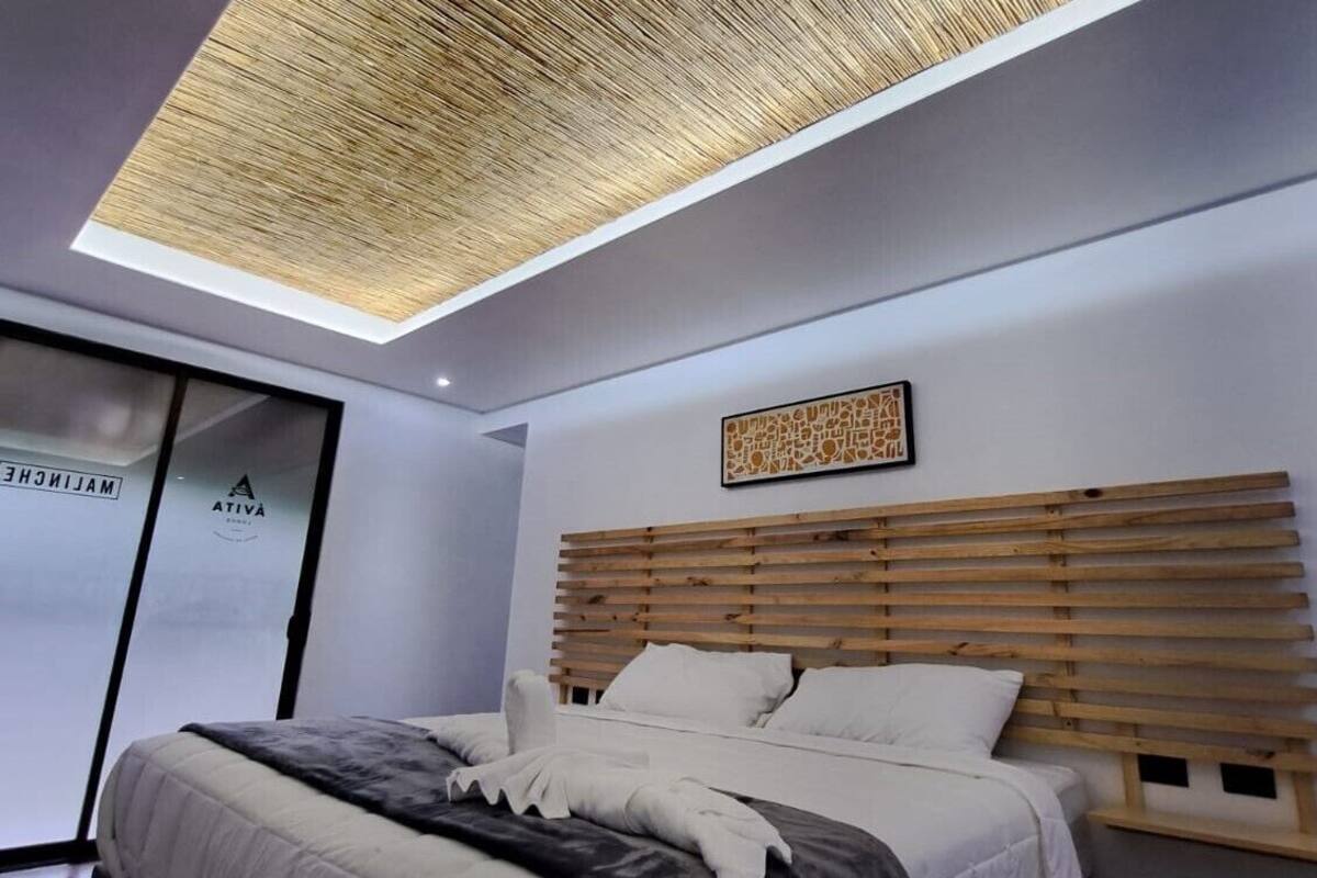 A modern bedroom with a wooden slatted headboard, a large bed with white and gray bedding, and a skylight above.