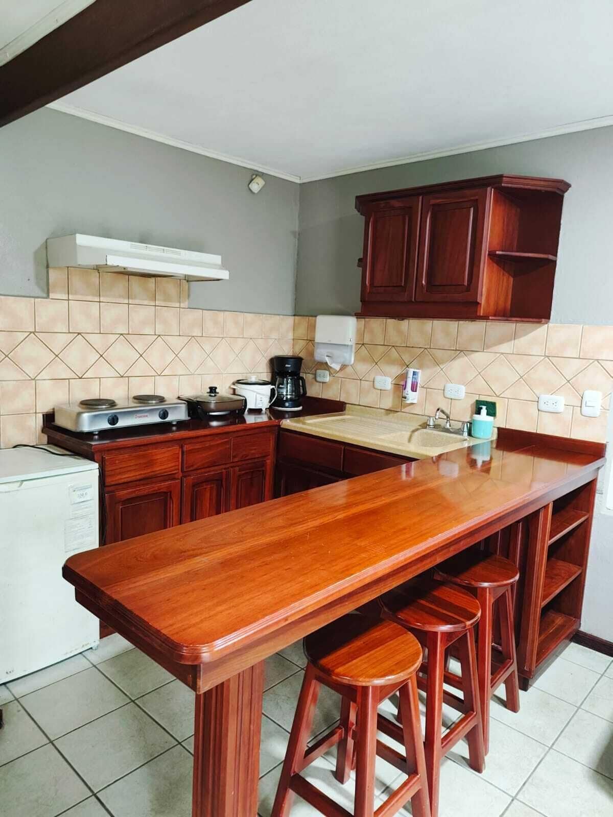 A kitchen with a wooden bar counter, stools, a coffee maker, and a refrigerator.