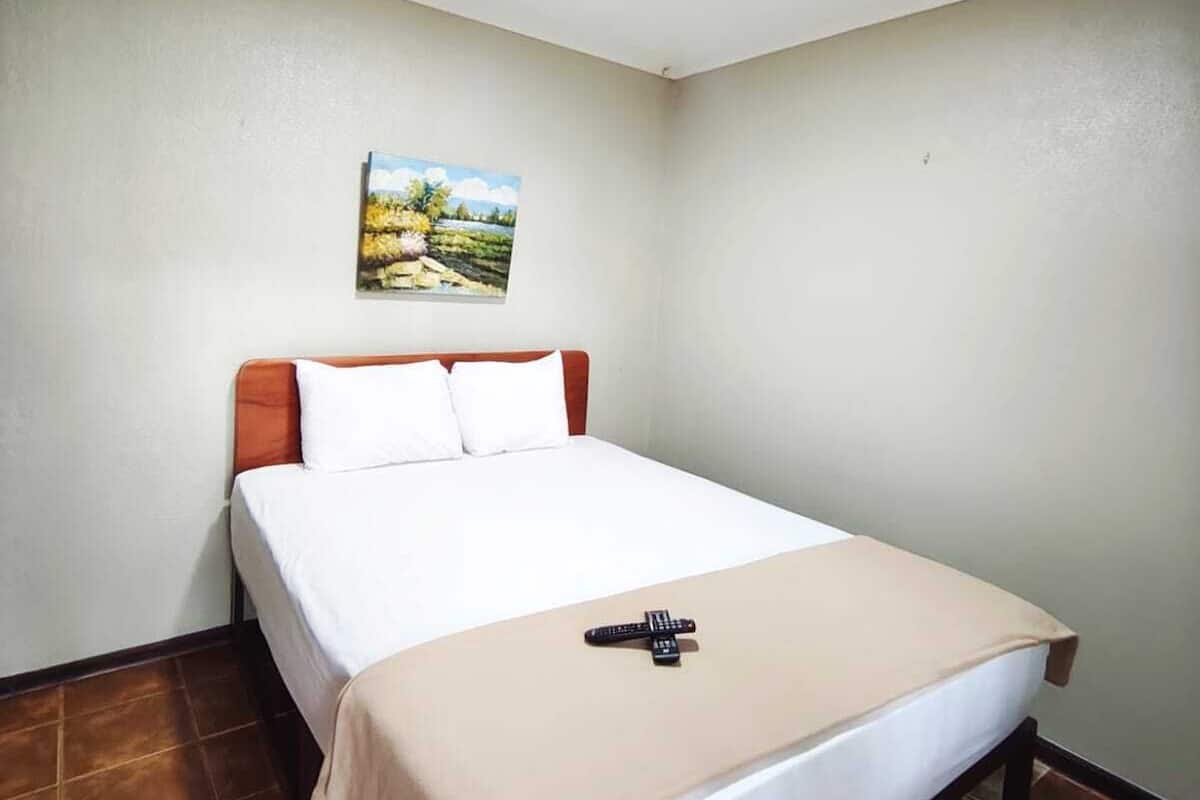 A single-bed room with a wooden headboard, white bedding, and a painting on the wall.