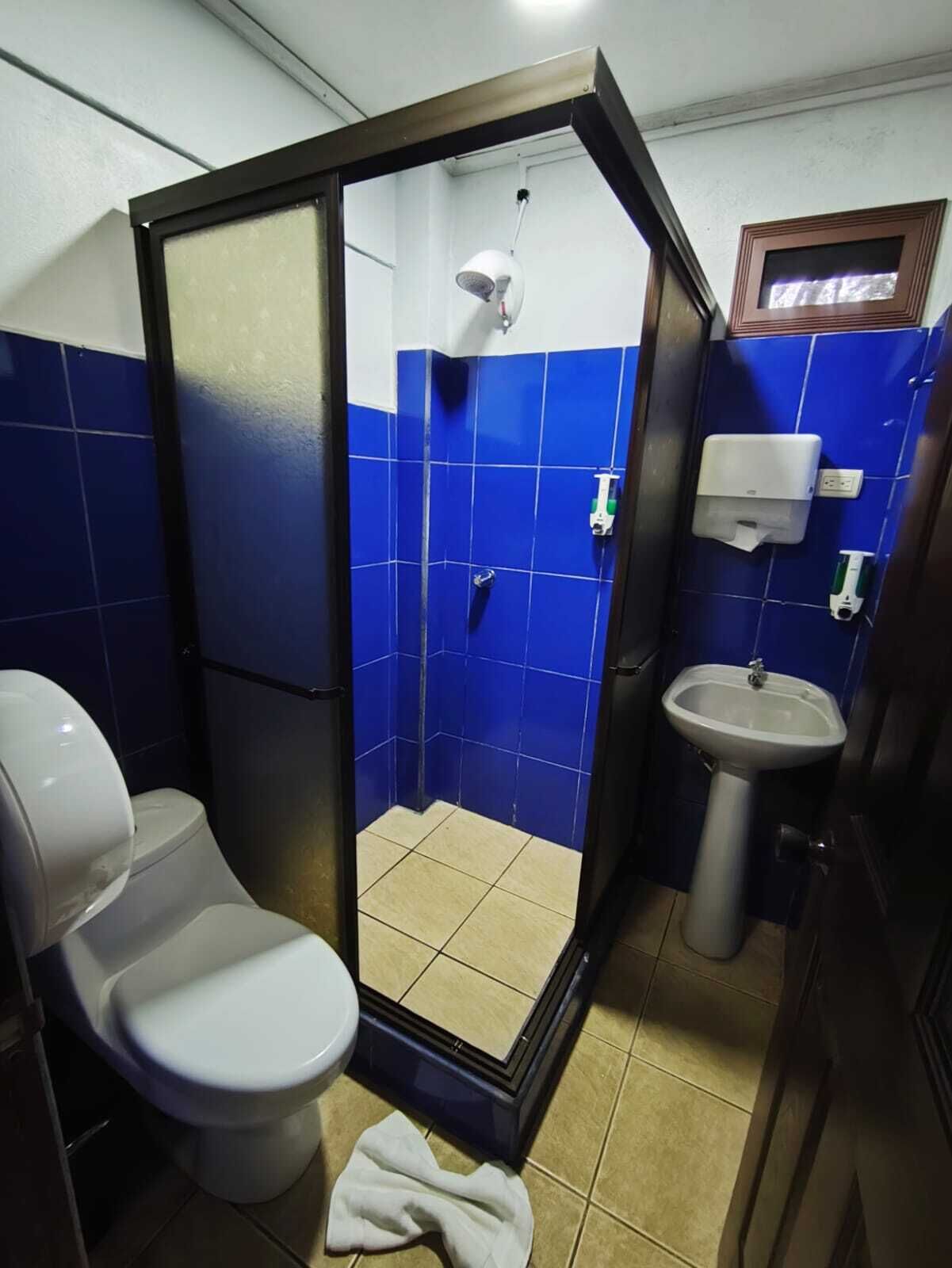 Un baño pequeño con azulejos azules, inodoro blanco, lavamanos y cabina de ducha.