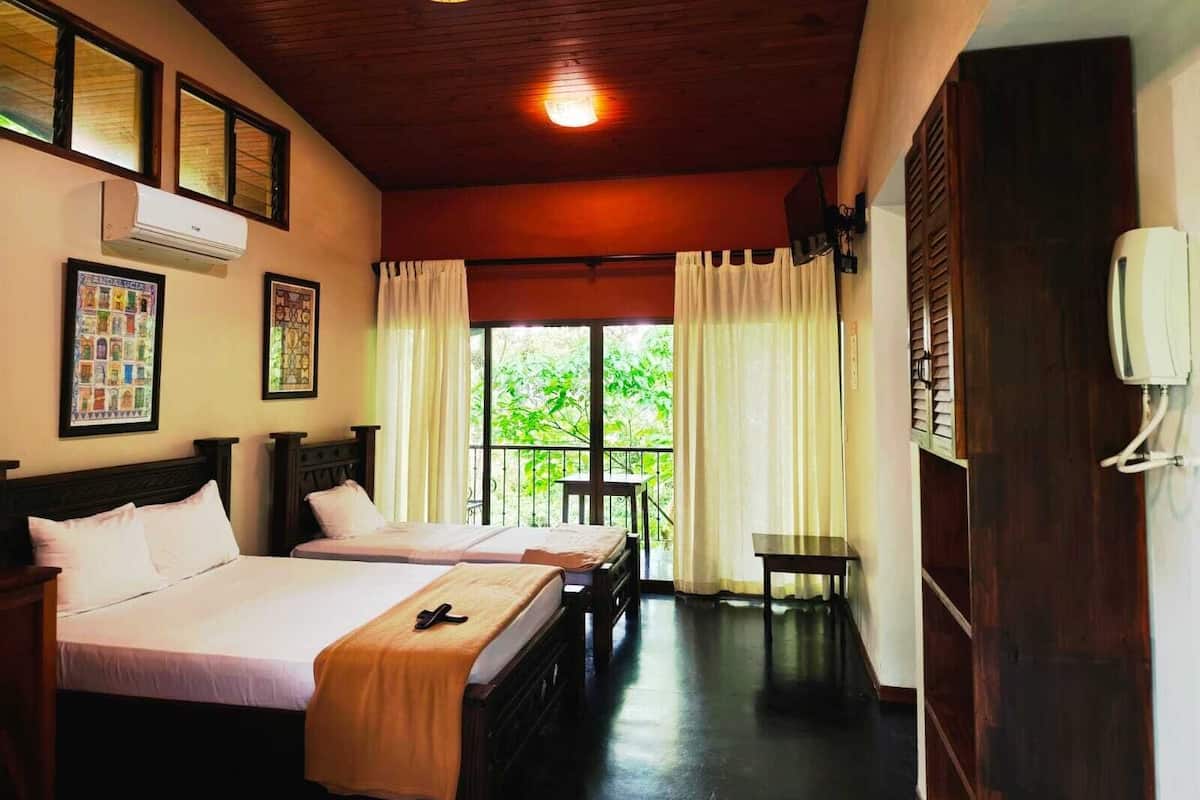 A hotel room with two beds, a small table, a ceiling light, and a window with curtains.