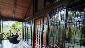 A wooden bench and a hanging chair on a covered porch with large windows and a door. - Avita Lodge Hotel de Montaña (Quesada)