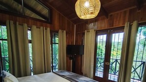 A wooden room with a large bed, a ceiling light, and windows with curtains. - Avita Lodge Hotel de Montaña (Quesada)