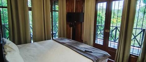 Una habitación con piso de madera, una cama grande, una lámpara en el techo y ventanas con cortinas.